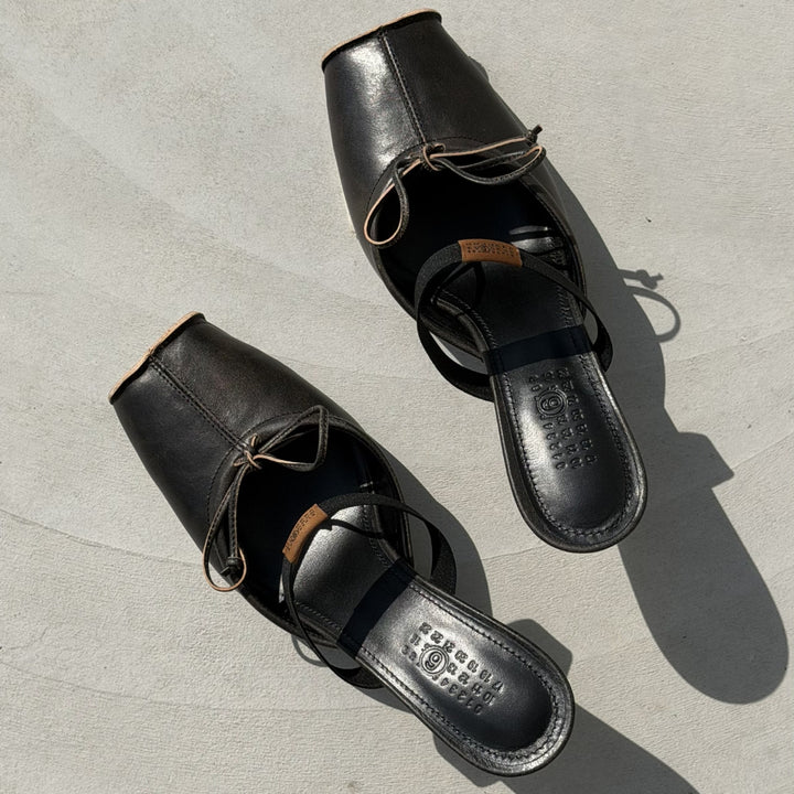 Pair of MM6 Margiela black leather slide sandals with lace detail on light surface