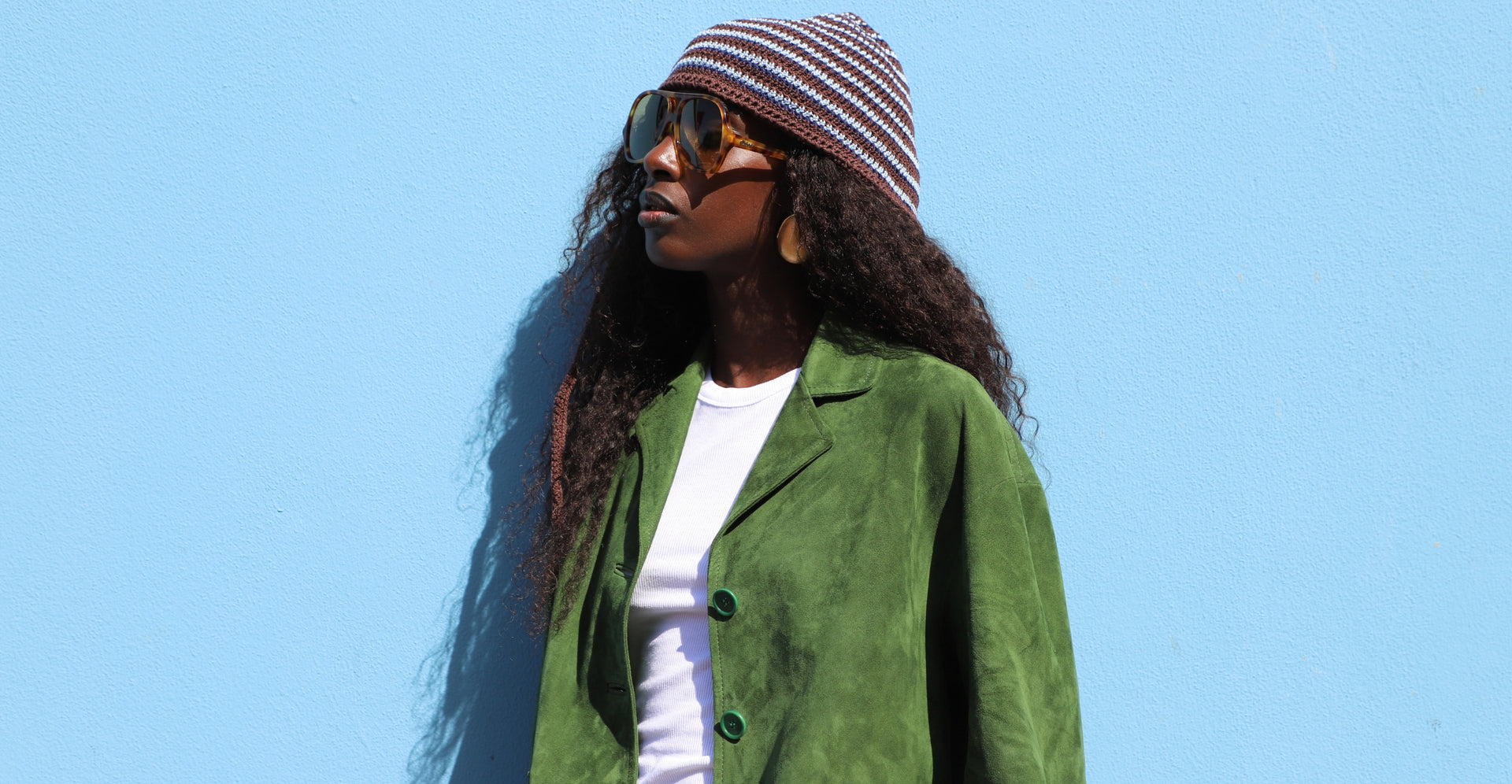 Colorful women's outfit featuring a green Santoro jacket, Chloé tortoiseshell sunglasses and a brown and light blue striped Miu Miu knit cap.