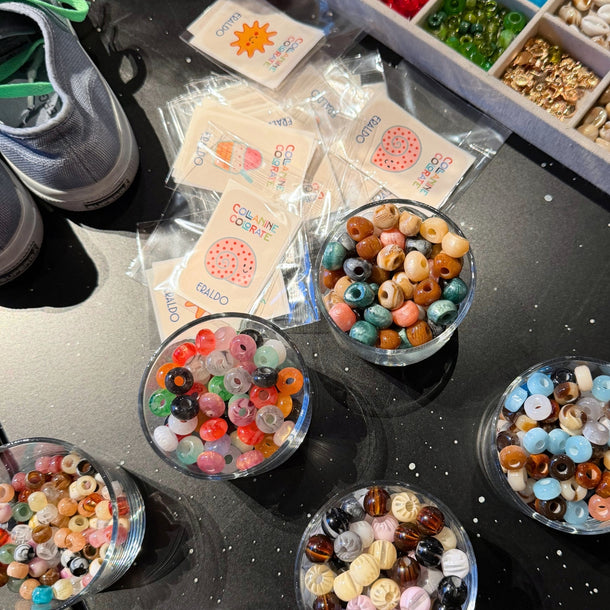 Colorful stickers and beads arranged on the workshop table for the Eraldo x Collanine Colorate sneaker customization event in 2026.