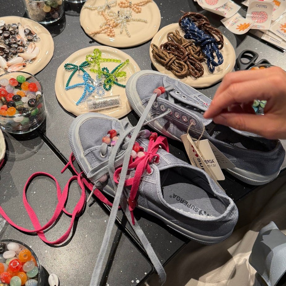 Grey Superga sneakers being customized with fuchsia laces and multicolor beads by Collanine Colorate during the 2026 Eraldo workshop.