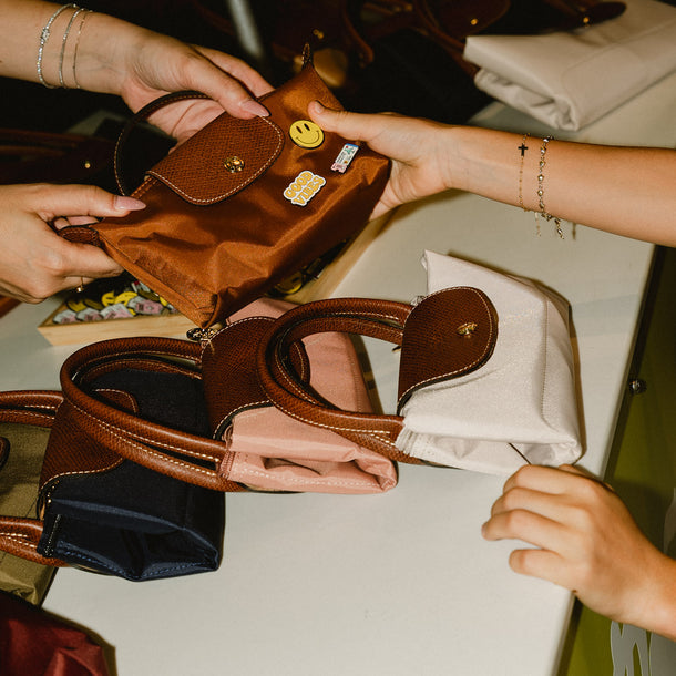 Customers personalizing iconic Longchamp Le Pliage bags with decorative pins during the AW26 event at Eraldo Store Jesolo.