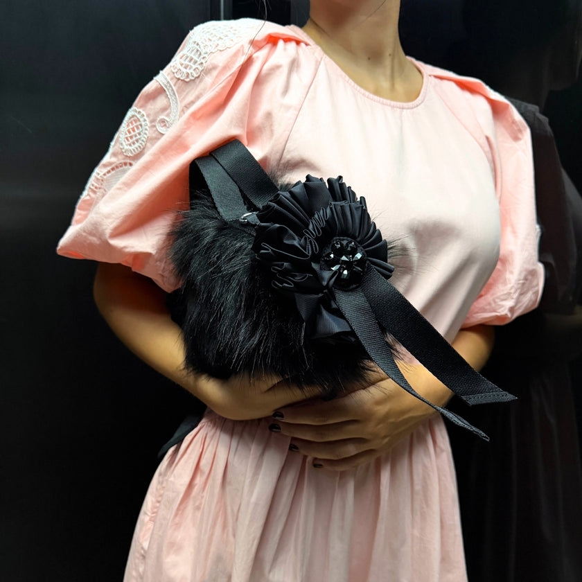 Model wearing a pink dress and holding a black Simone Rocha faux-fur bag with rosette detailing and crystal embellishment.