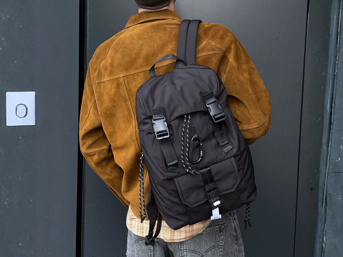 Men's New Arrivals 26 featuring an A.P.C. black backpack worn with a Studio Nicholson brown suede jacket.