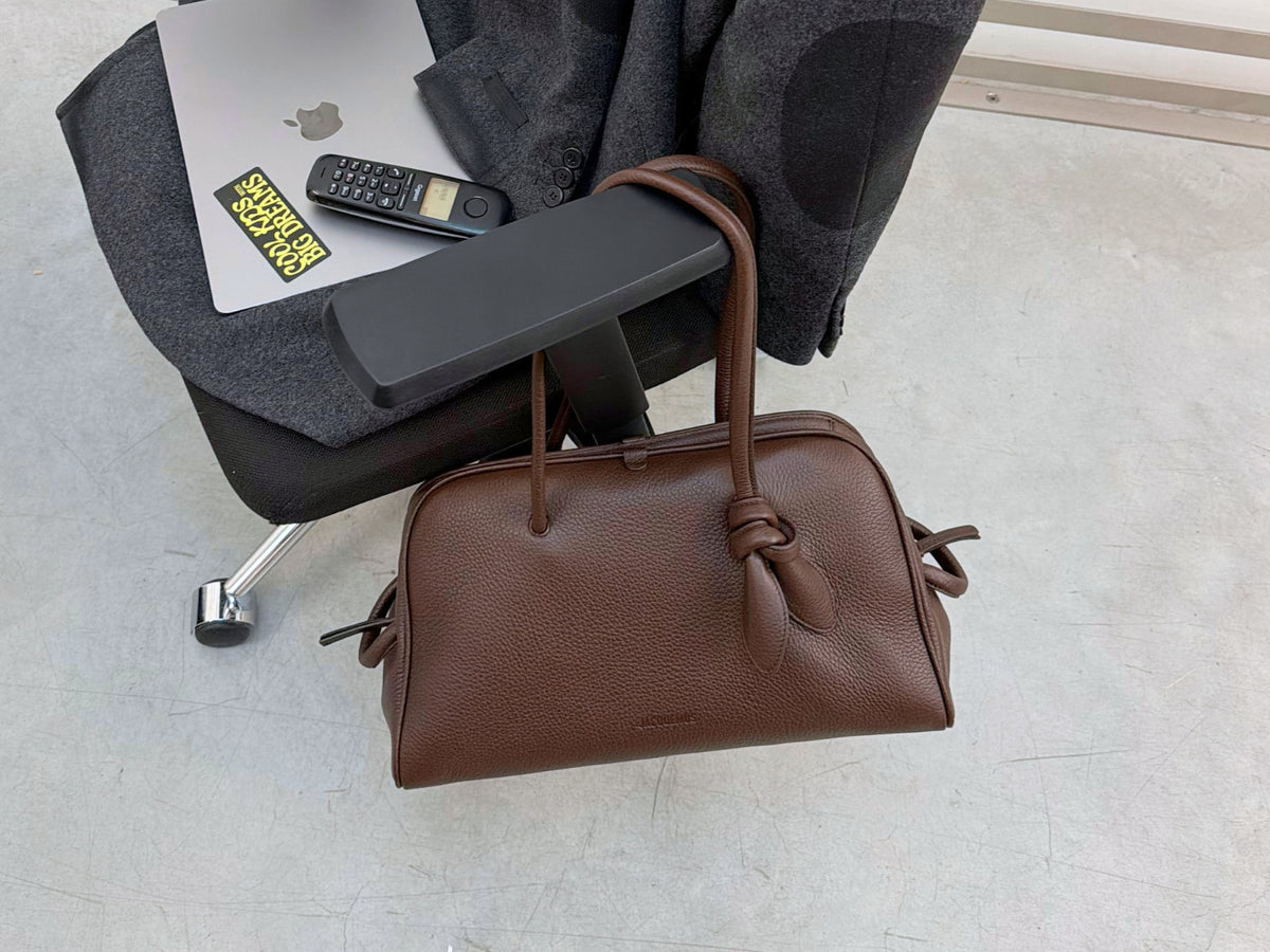 Men's New Arrivals 26 featuring a large brown Jacquemus leather bag placed on an office chair.