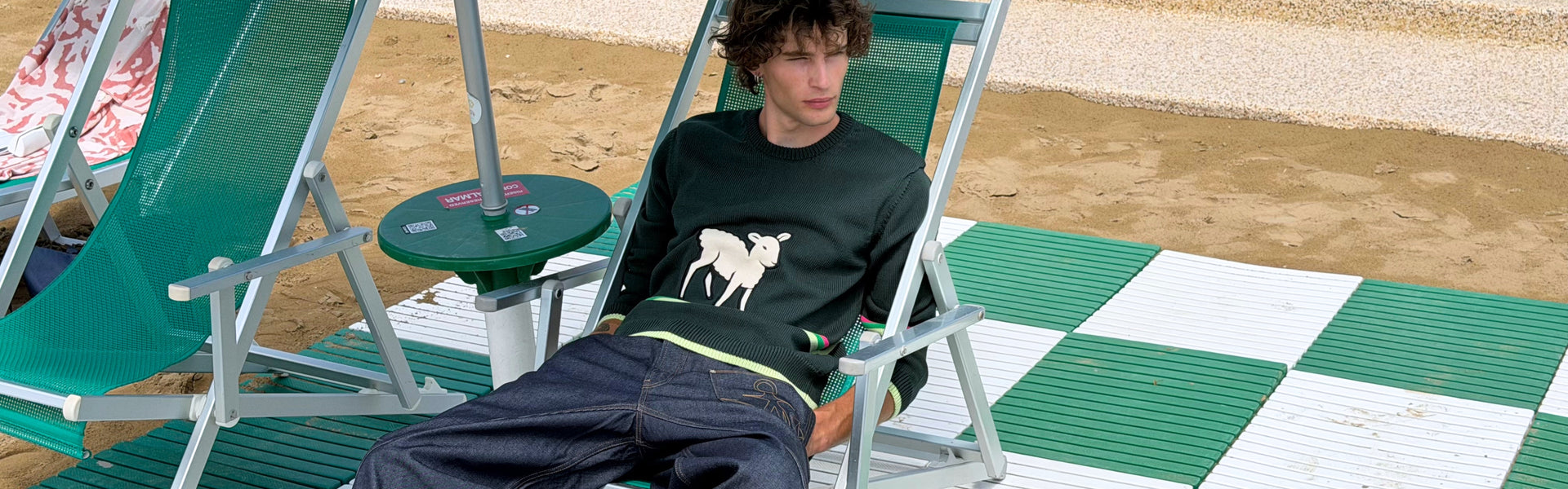 Men's New Arrivals 26 featuring a JW Anderson forest green sweater and dark blue jeans on a beach