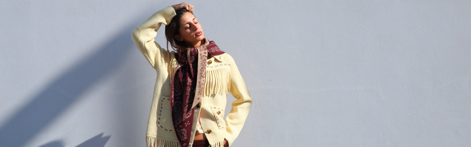 Model wearing a cream fringed Guest in Residence knit jacket with button closure and a brown Lemaire knit skirt.