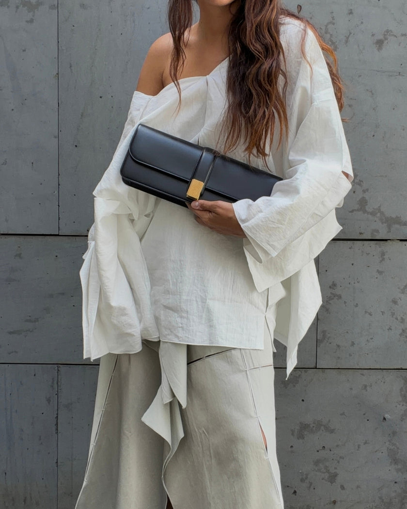 Woman wearing a white oversized shirt and grey maxi skirt by Niccolò Pasqualetti with a black bag by Khaite