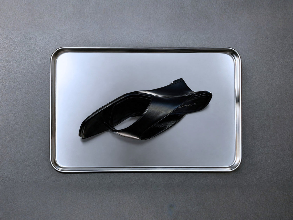 Stuart Weitzman black wedge-heel flip-flop sandal displayed on a silver tray